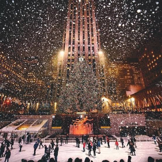 a nighttime shot of the iconic ice skating rink in front of the Rockefeller Center tree in New York City with snow falling