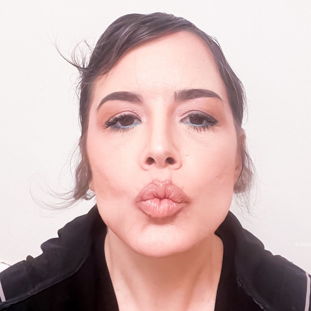 This is a headshot of me wearing a very nice make up look from a professional make up artist who prefers to not reveal her name. In this shot I am lit by a pink lightbulb and my complexion tones are pinks. The interesting thing the artist did with the make up on my eyes was a nice brow shape and brown color, some blush colored eyeshadow with black mascara and a robins egg blue Anastasia Beverly Hills eyeline on my lower lid. I’m making a kissy face wearing a blush colored lipstick I believe is Chanel’s baume that looks like Marylin’s rouge allure under amber light which I thought was fun. I might have the brands wrong. I tried, sorry.