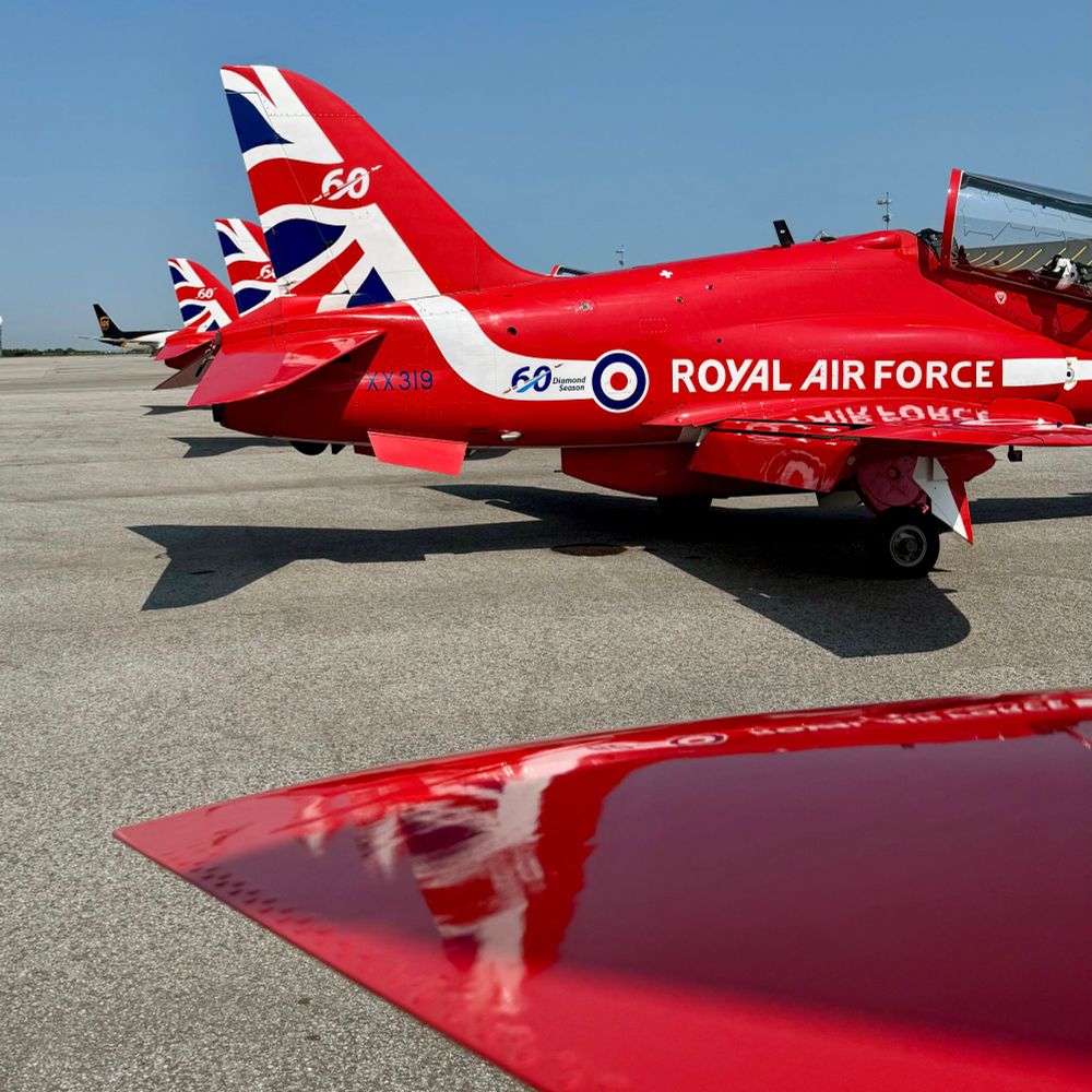 The 60th Anniversary tail markings of a RAF Red Arrow jet reflected on the horizontal stabilizer of another Hawk jet.