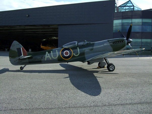 A vintage WW2 Spitfire outside in front of a hangar. 