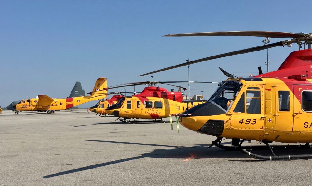 Three RCAF Search and Rescue painted CC-146 Griffon helicopters in front of a DHC-5 Buffalo and C-130 Hercules, all in a row. 