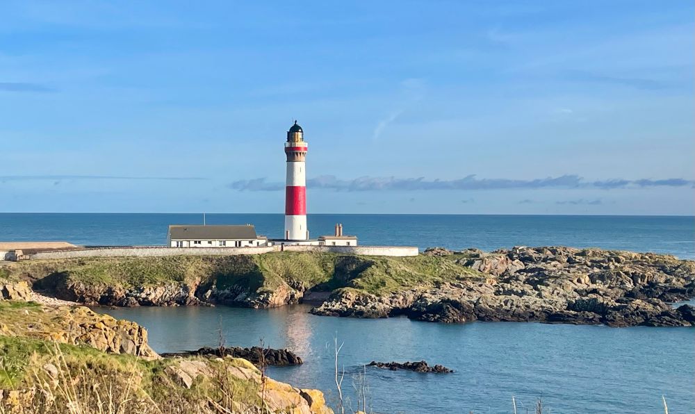 Red and white striped lighthouse on a small island at Boddam with smooth water surrounding it