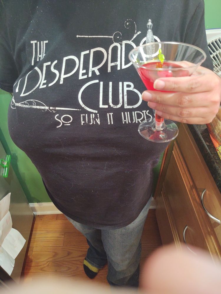 Woman holding a Shirley Temple with two cherries. She is wearing a Desperado Club T-shirt.