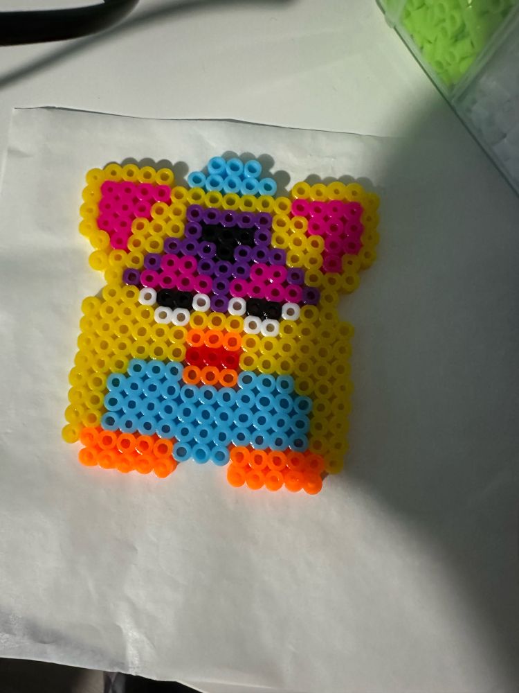 A Furby of various colors made out of perler beads against a white background