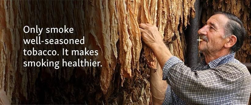 A tobacco farmer with a lit cigarette in his mouth examines drying tobacco leaves. A caption says, “Only smoke well-seasoned tobacco. It makes smoking healthier.”