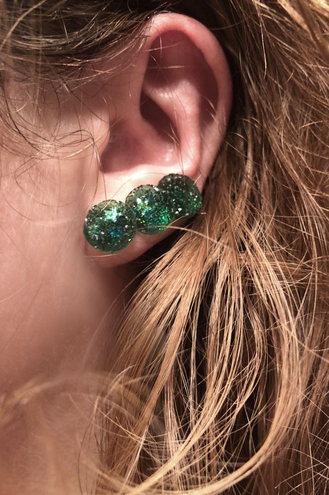 Picture of a woman's ear with 3 green earrings