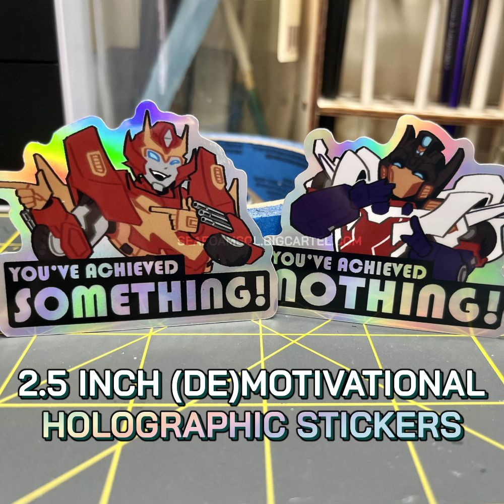 Photograph of two 2.5 inch holographic stickers, featuring Rodimus and Getaway from Transformers IDW 2005. Rodimus is shooting two finger guns and a wink, and the text under him reads "YOU'VE ACCOMPLISHED SOMETHING!" Getaway is pointing and laughing, and the text under him reads "YOU'VE ACCOMPLISHED NOTHING!" The background is of miscellaneous art supplies.