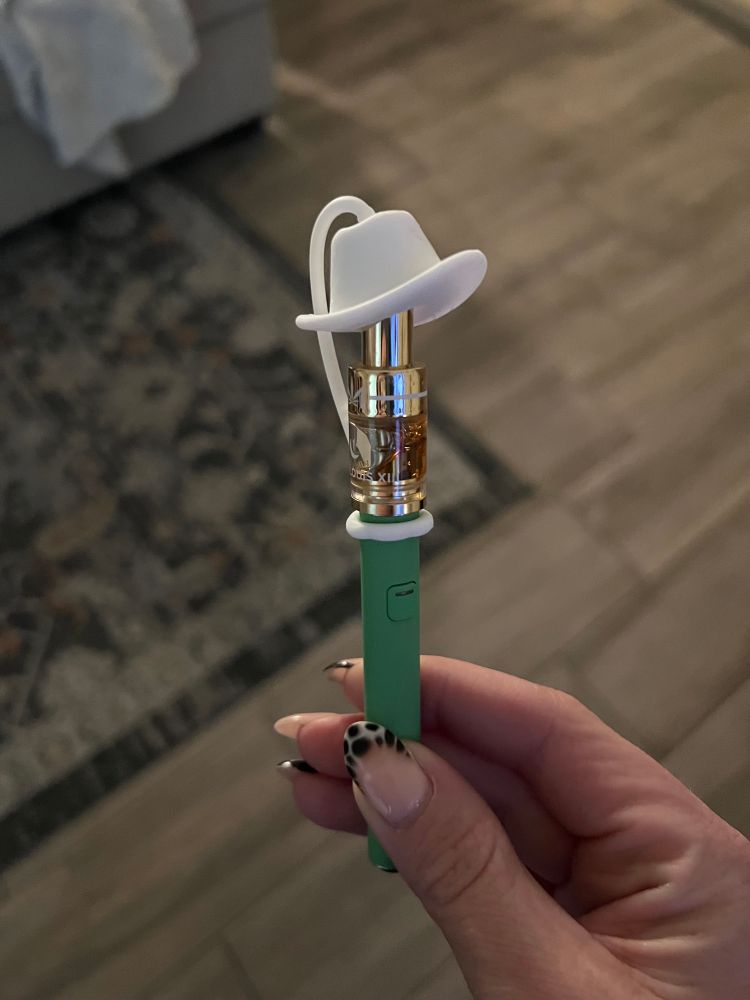 a hand holding a weed pen with a cowboy hat shaped straw cover on the end
