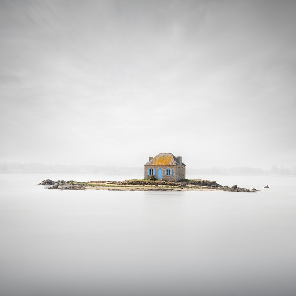 Minimalist photo of an old stone house on a small island in Brittany (France). Long exposure smoothed out the water surface and partly the clouds.