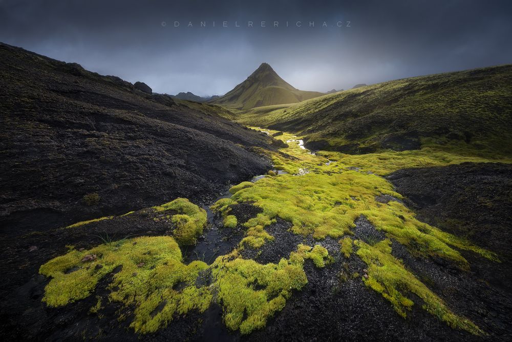 The southern interior of Iceland. The highlands here are full of contrasts of dark volcanic landscapes and light green mosses as seen in the photo. The foreground is formed by interesting shapes of fresh moss and in the background towering mountain peaks. Dark heavy clouds add to the mysterious atmosphere.