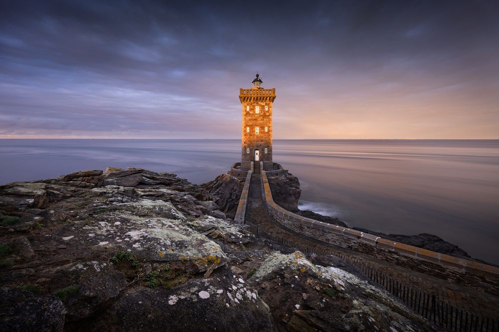 Beautiful morning on the wild coast of Brittany (France) at the lighthouse Le Phare de Kermorvan. The lighthouse and the dark sky are beautifully illuminated by the first light.