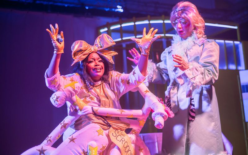 Laura Lovemore in a bizarre outfit, like a sausage dog wrapped-up in Christmas paper, as Ghost of Christmas Present with Graham Crammond as Dame Scrooge