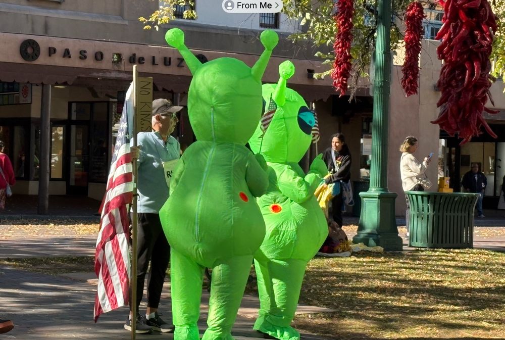 2 green space aliens getting ready to join the No Kings march from the Plaza in Santa Fe.