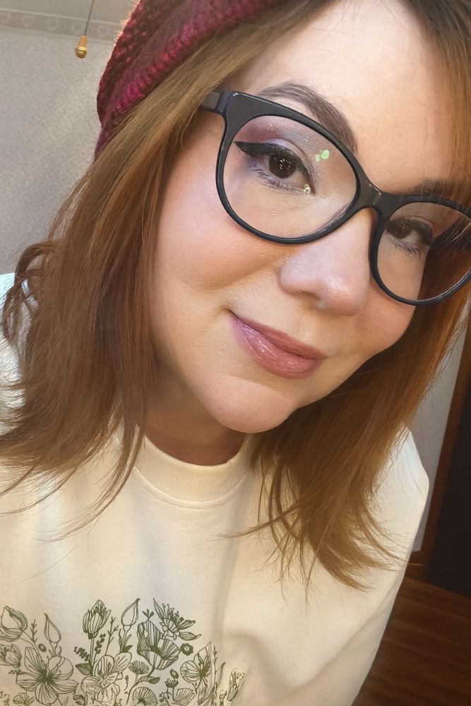 A selfie showing up my sort of frosty make up. I’m reading a slouchy red beanie, pink/blue frosty eyeshadow & black winged eyeliner with think framed glasses 