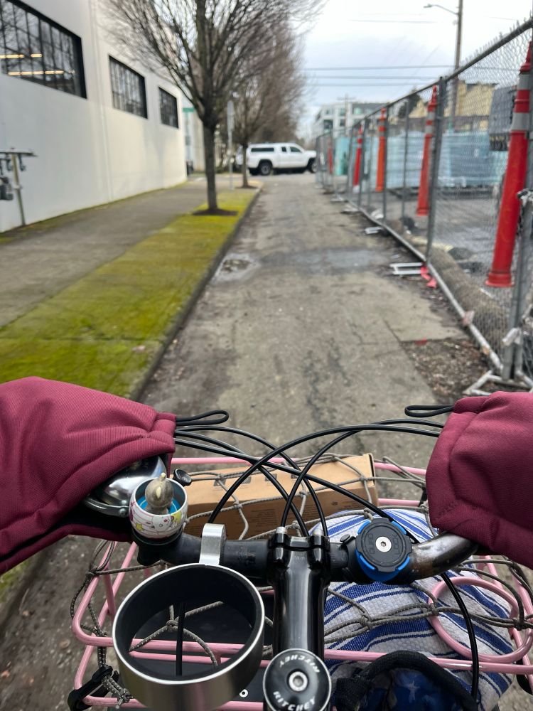 View of front bike basket and portion of handlebars in a narrow road with construction fencing on one side