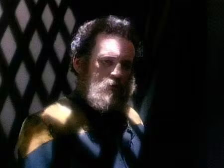 Chief of engineering Miles O'Brien, looking forlorn, in a dark cell with an unkempt beard. 