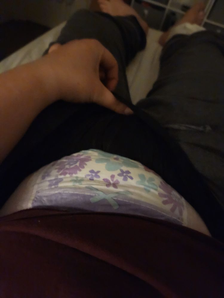 A PoV picture showing a hand holding out the waistband of pajama pants, revealing a goodnites diaper with purple flowers