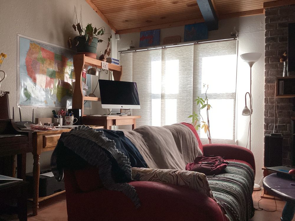 Sun lit window behind a scene of desks, an iMac, a couch, and a US map on the wall.