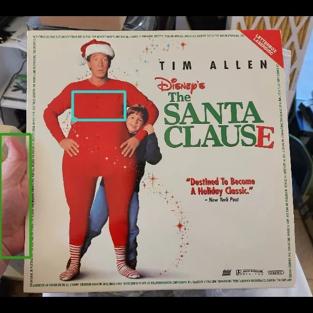 A photo of the laserdisc cover for Disney's The Santa Clause, featuring Tim Allen in a red onsie.
There's a blue box around his "breasts", and a green box around the hand on holding the laserdisc 