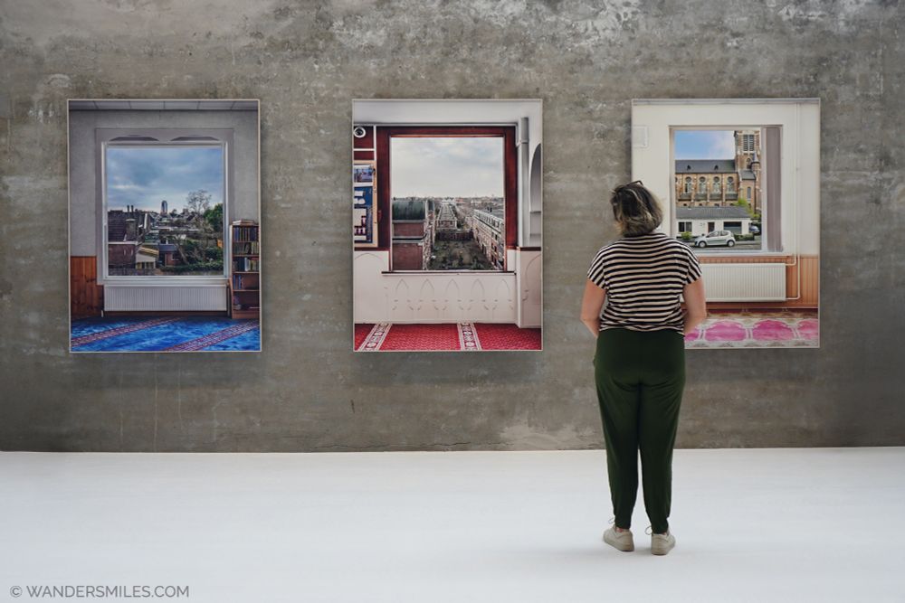 woman looking at a triptych of painting on a grey wall at Fenix Museum of Migration in Rotterdam
