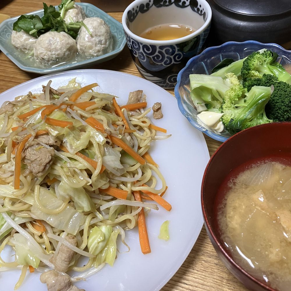 焼きそば、味噌汁、茹でブロッコリーサラダ、肉団子、湯飲みに入ったお茶が並ぶ和風の家庭料理の食卓。