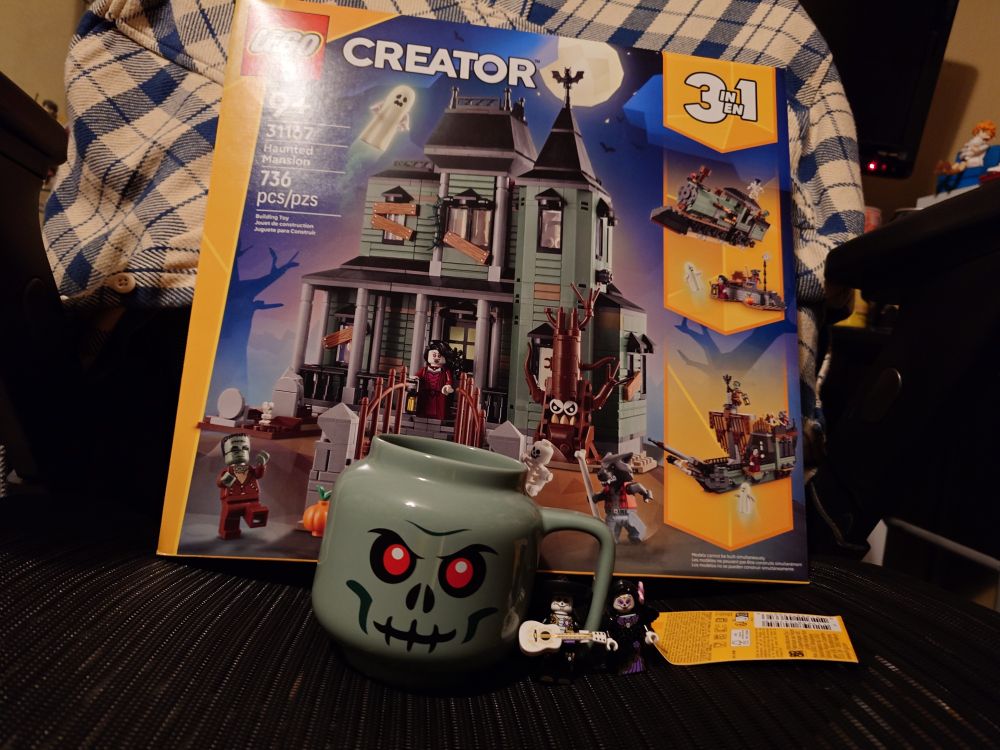 A Lego haunted House set, Lego zombie skull mug, and two dia de los muertos minifigures on the seat of a mesh chair. 