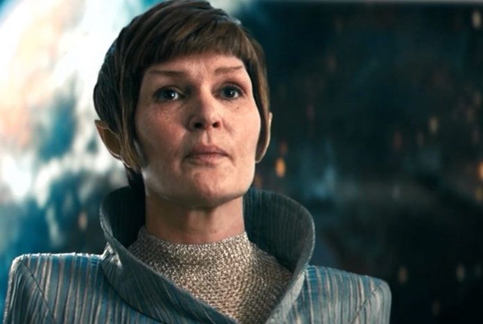 A woman looks across the room. She has a Vulcan hair cut, pointy ears, a space gown on, and a look of thoughtful determination on her face. 