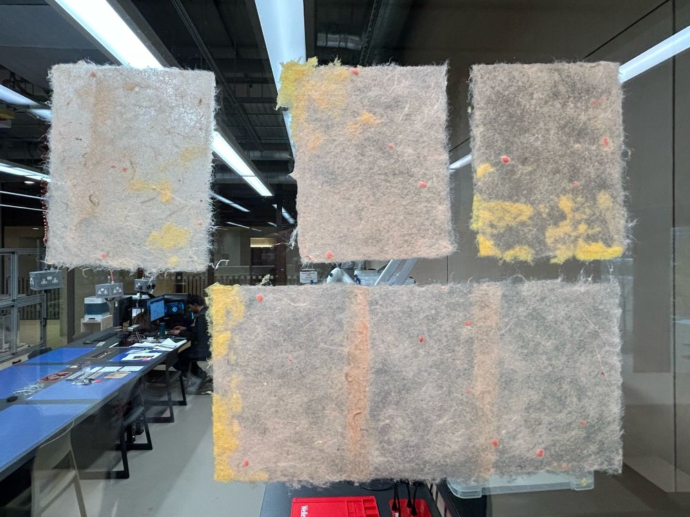 Mixed handmade papers drying on a window. The papers are a very pale pinkish orange. All are flecked with orange-red fibres, and layered with yellow pigmented cotton in sections. 
