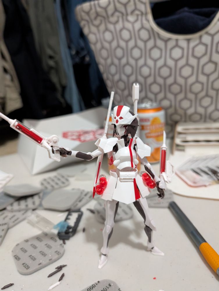 Picture of a white and red figure maid from a model kit. It's surrounded by several tools and sanding pads used to make it.