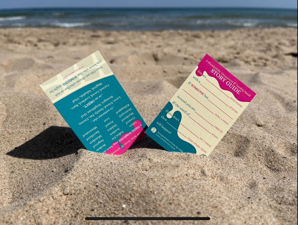 Front and back of A Wonderfully Unexpected & Terribly Small Story Guide stuck in sand at a beach (the back one is inexplicably upside down)
