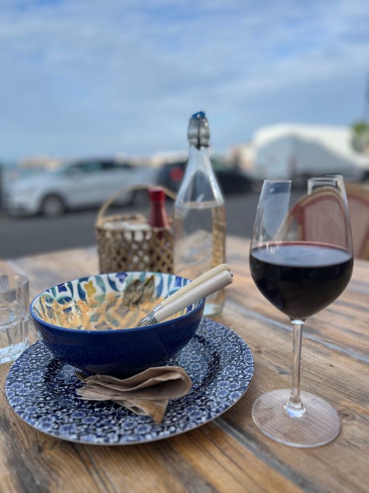 An empty bowl that had a delicious Thai red curry in it and a half-drunk glass of red wine on an outside table under a blue evening sky