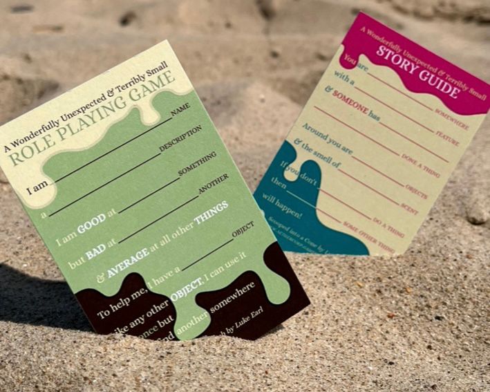 Two business cards stuck in sand with a melting ice cream design, one titled Role Playing Game, the other Story Guide