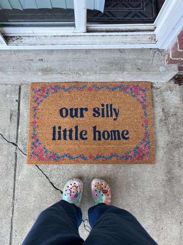 brown doormat that reads “our silly little home” with a flower border