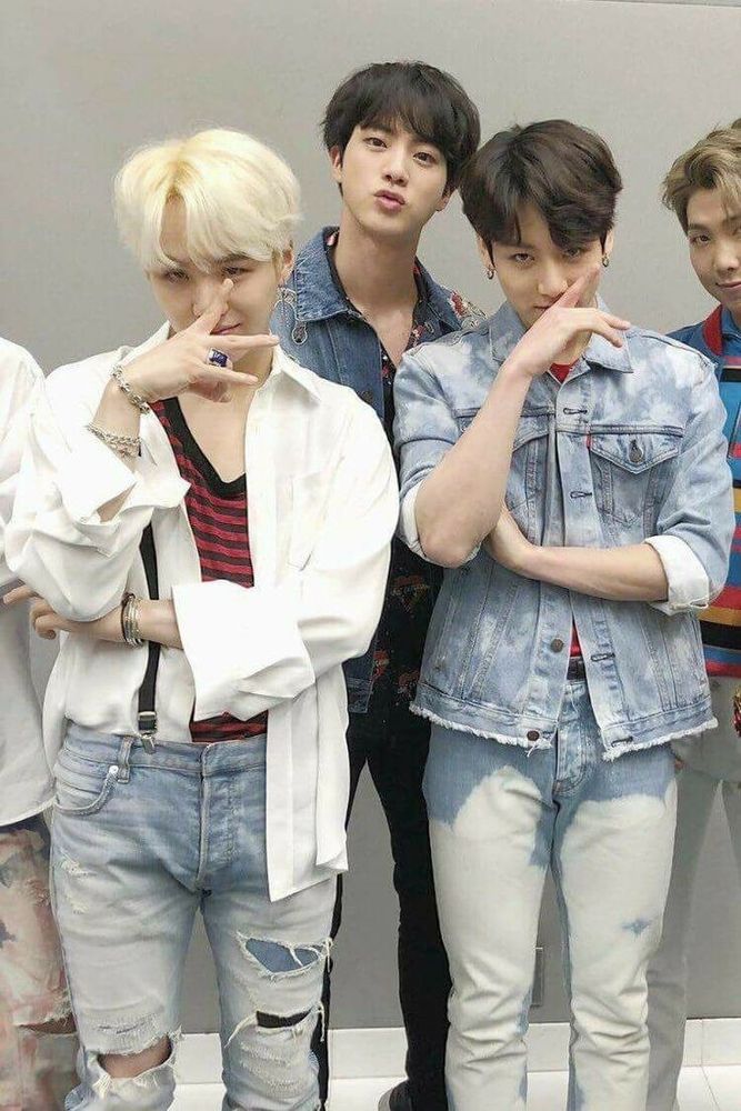 Yoonkook in ripped, partially acid wash jeans. They are partially covering their faces with their hands and Jin is standing behind them looking out from between them.