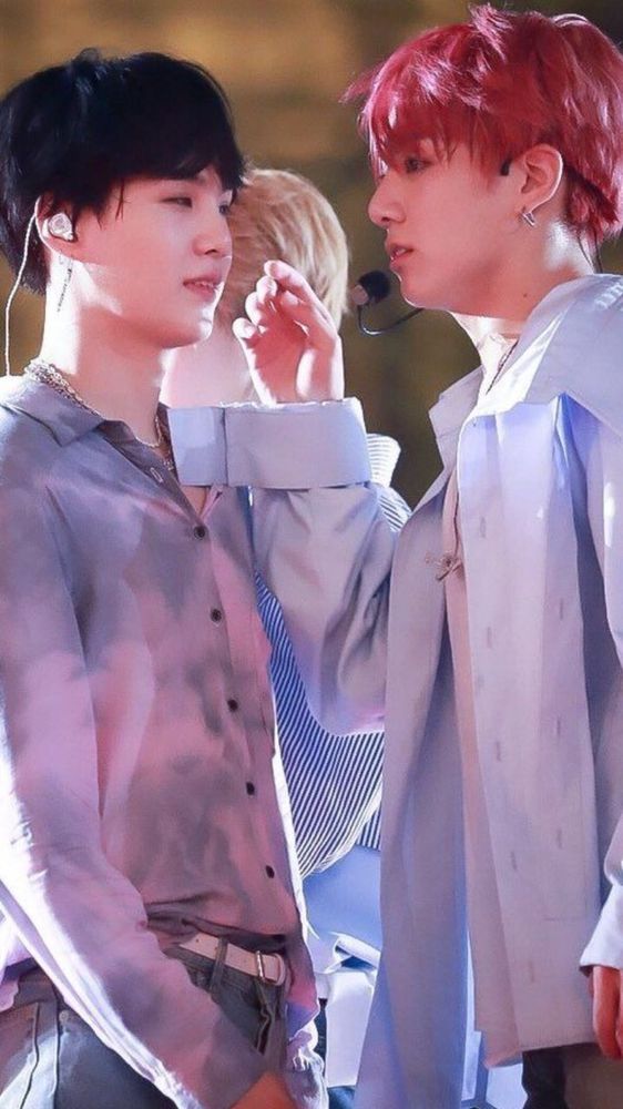 Yoonkook on stage in pastel clothing. Jungkook has his hand up like he's about to whisper a secret to Suga.