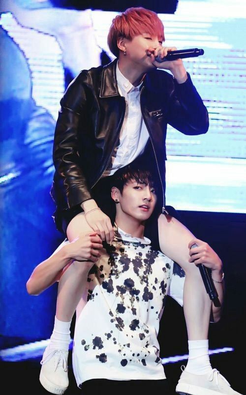 Yoongi, in shorts and a leather jacket, riding in Jungkook's shoulders as they perform on stage.