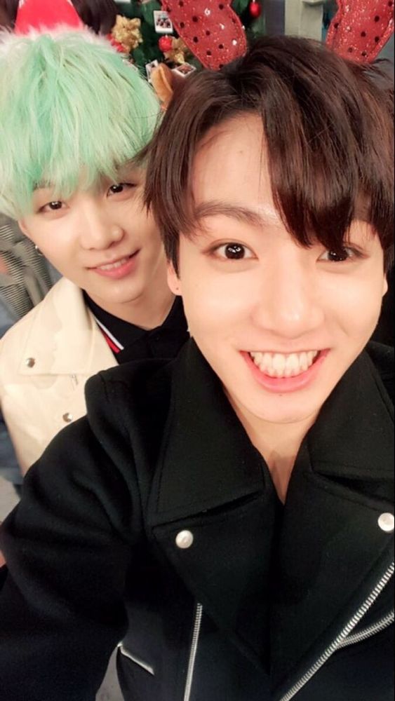 A Yoonkook selfie with red sparkly antlers. Suga has mint green hair and Jungkook is smiling with all his teeth 