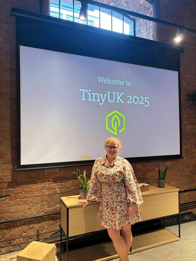 Woman standing in front of a screen that says “Welcome to TinyUK 2025” in a cool converted factory-turned-event space 