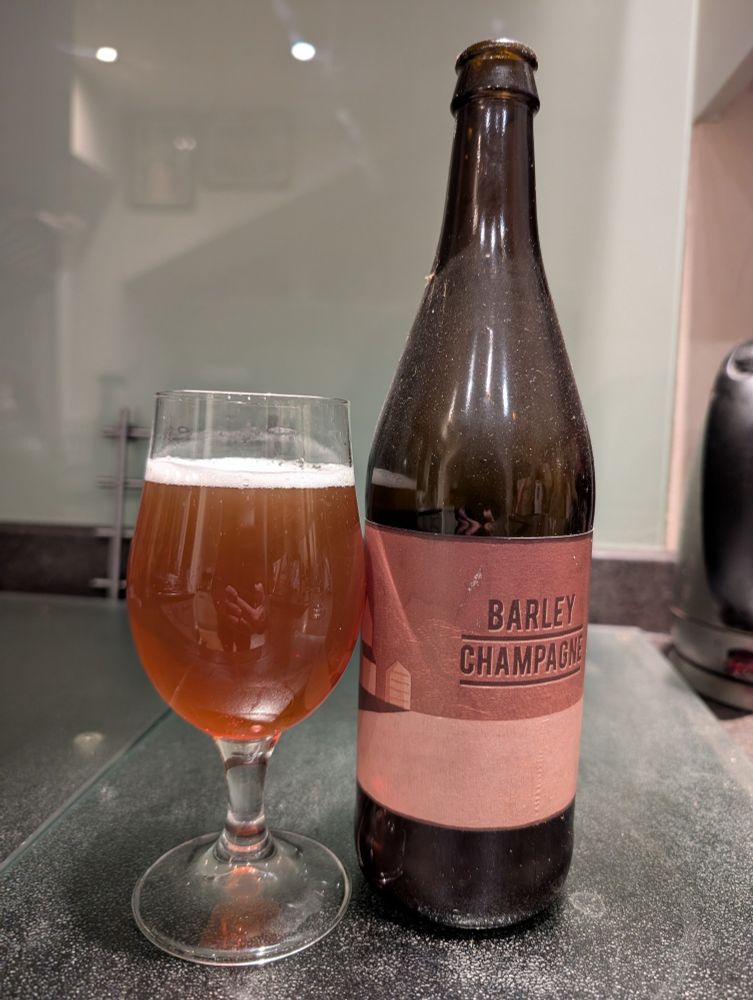 A bottle of Beavertown Barley Champagne with a tulip glass of amber liquid with a small white head.
