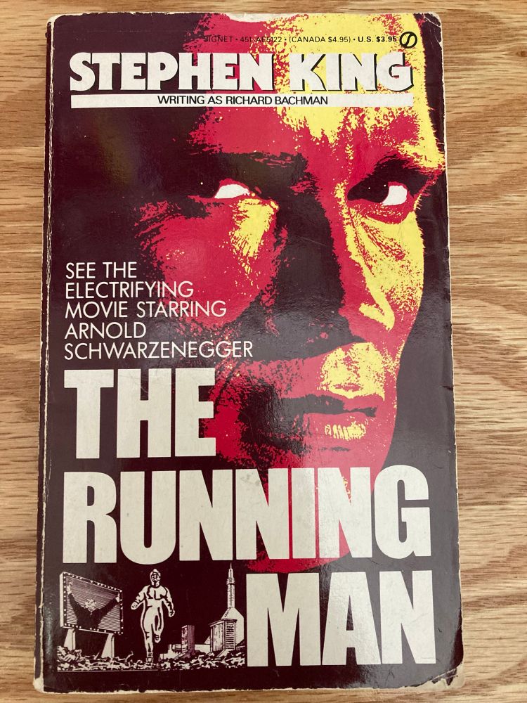 Book cover of The Running Man by Stephen King, writing as Richard Bachman. Arnold Schwarzenegger’s face is at the center, and all caps alt text reads: “see the electrifying movie starring Arnold Schwarzenegger”