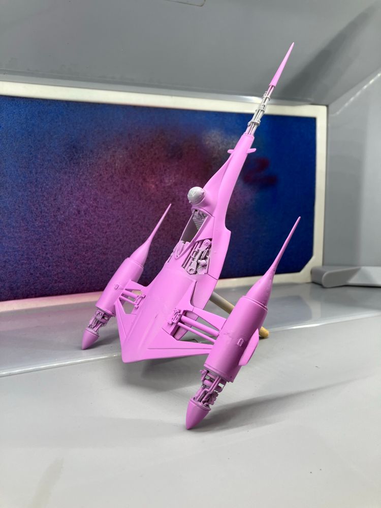 A modified model of a Naboo starfighter. It is painted almost entirely in pink, and is resting in a desktop spray booth. 
