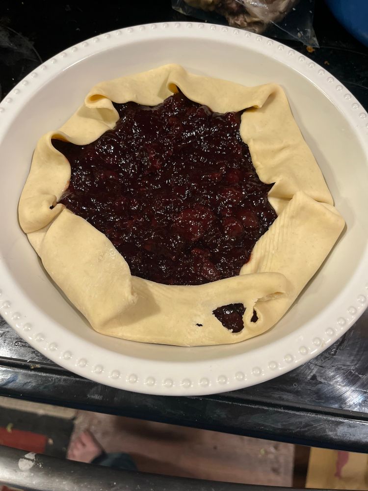 A deep pie dish with an unbaked cherry crostada inside. 