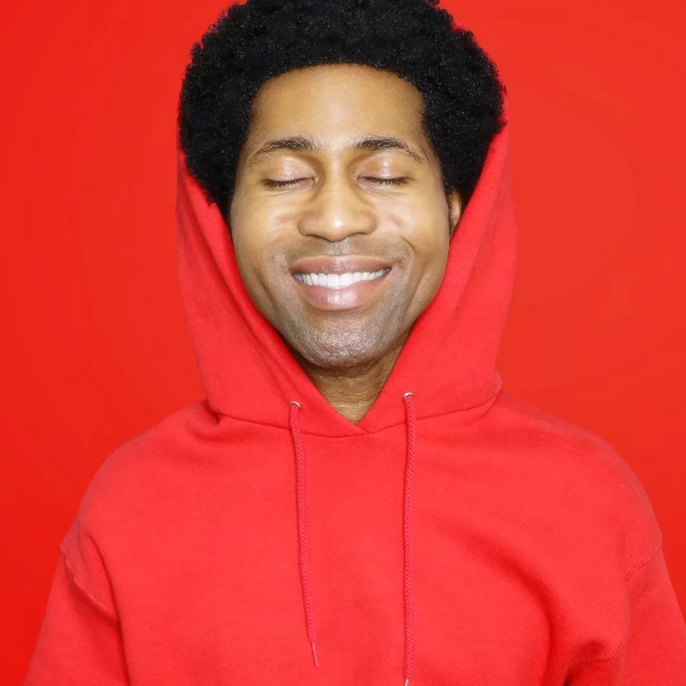 A man in a red hoodie smiling in front of a red background