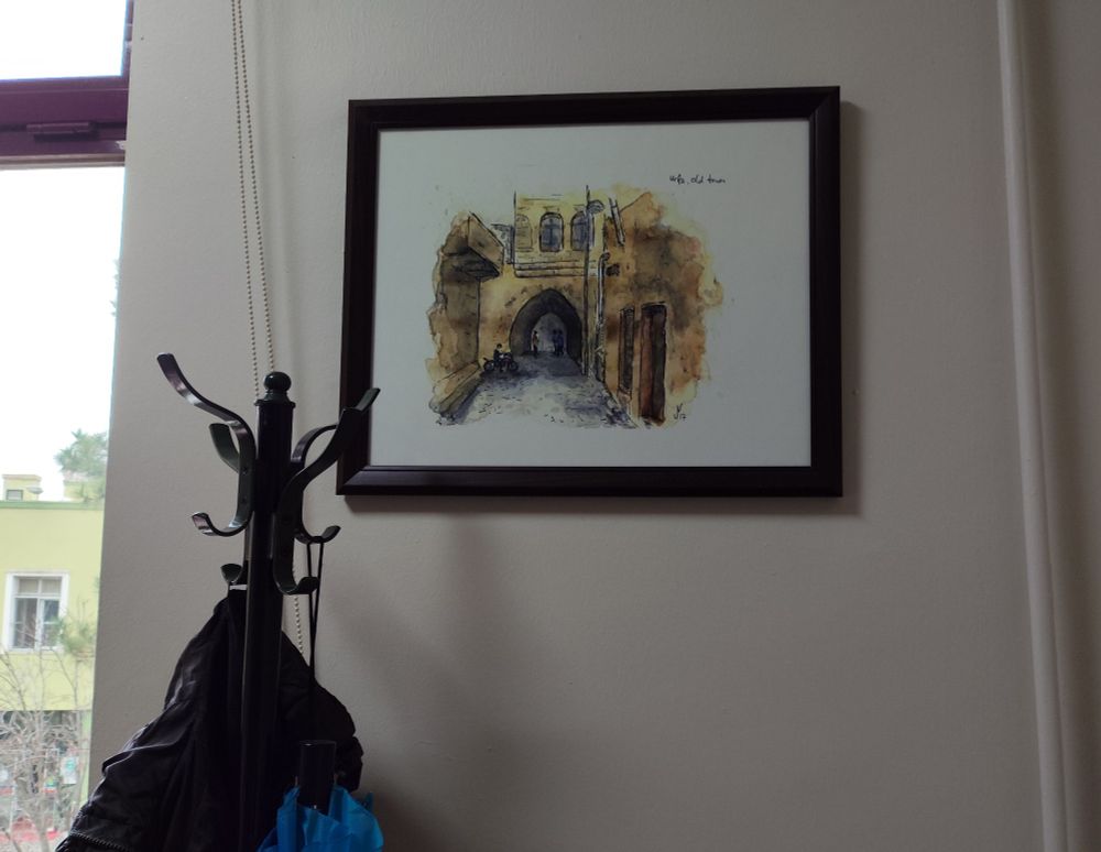 A framed sketch of @jensnotroff.com hung on a wall, showing an old alley in Urfa's old town, purchased from https://www.redbubble.com/people/fieldsketches/shop.