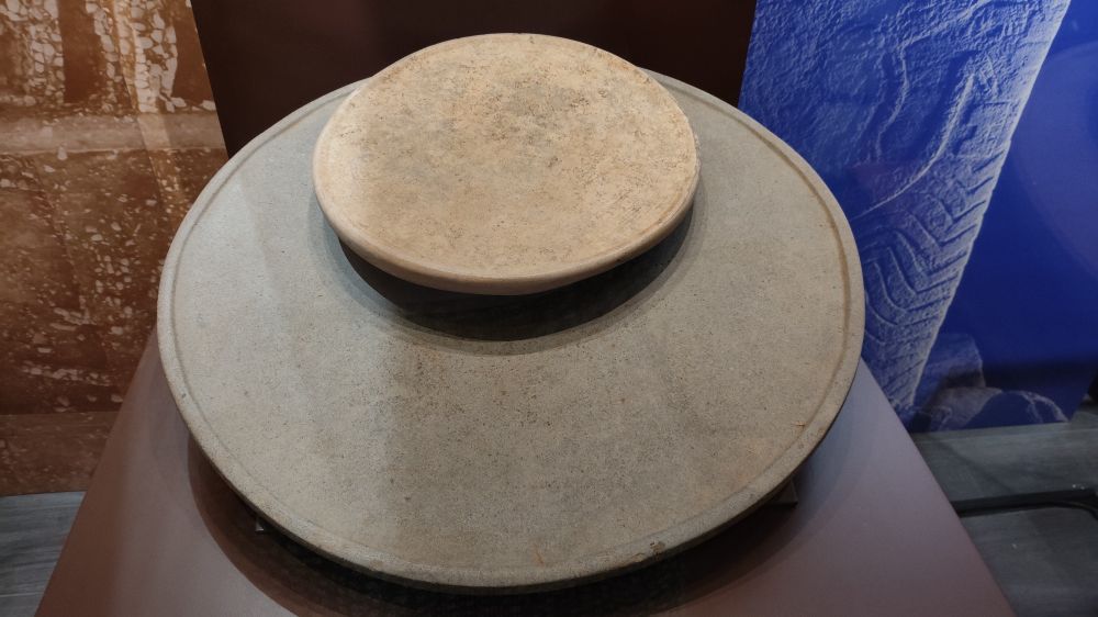 Two stone plates one on the other, round like discs, the edge of the bigger one has a slightly elevated rim.
 One is about 50 cms in diameter, the other is about 20.