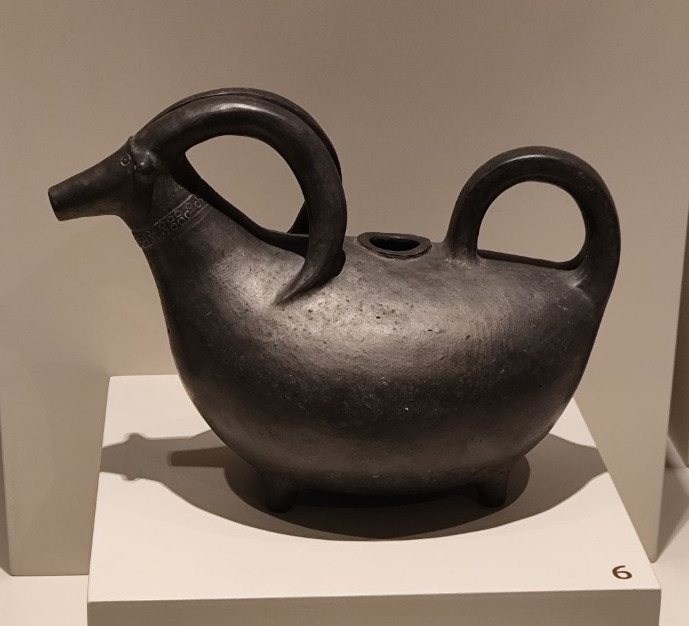 A black clay jug in the form of a goat. The tail and the horns have been made as cusps.