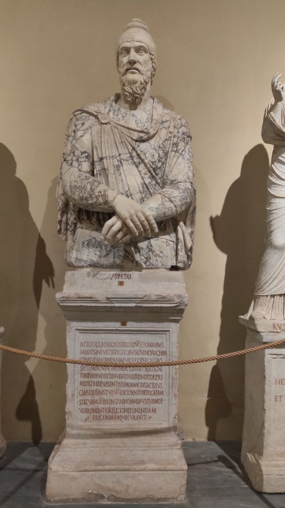 The upper side of the body of a bearded man wearing a chiton and a Phrygian cap, hands clenched in front