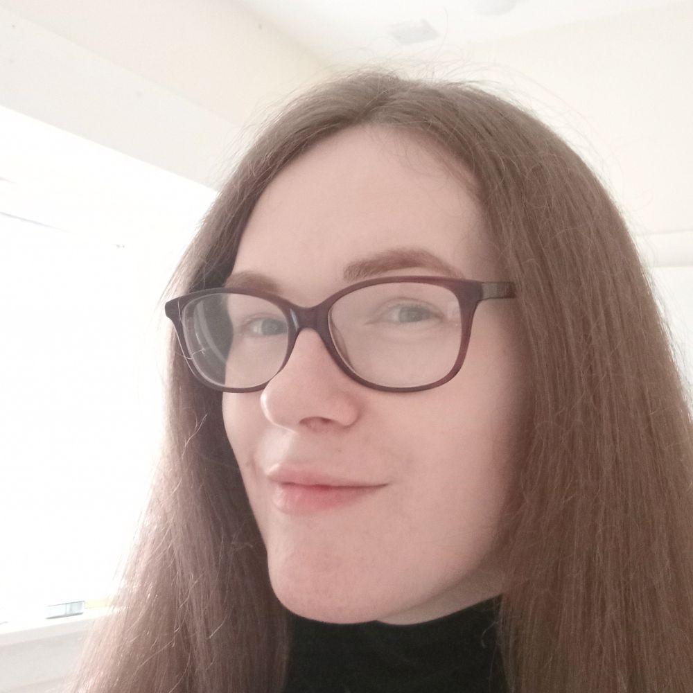 A photo of a smiling, pale, brown haired woman.  She is wearing a black choker and purple glasses, and is set in front of a bright window.

She is very happy with the shape of her lips, which are more plump and have a noticeable cupid's bow.