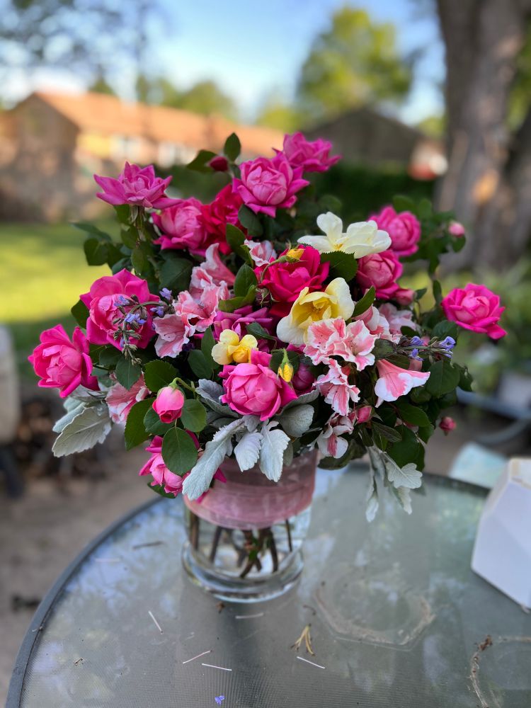 A large bouquet of pink and yellow roses in a vase. A little sprig of coral and white azalea and sage and dusty miller thrown in for extra texture and interest. 