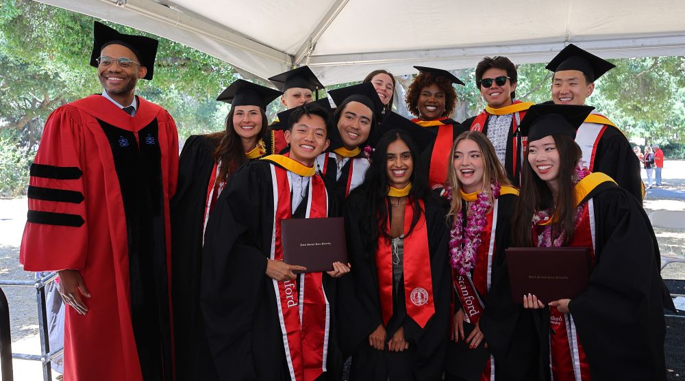 A group of coterminal MA graduates smiling for a photo with the faculty director of the MA program
